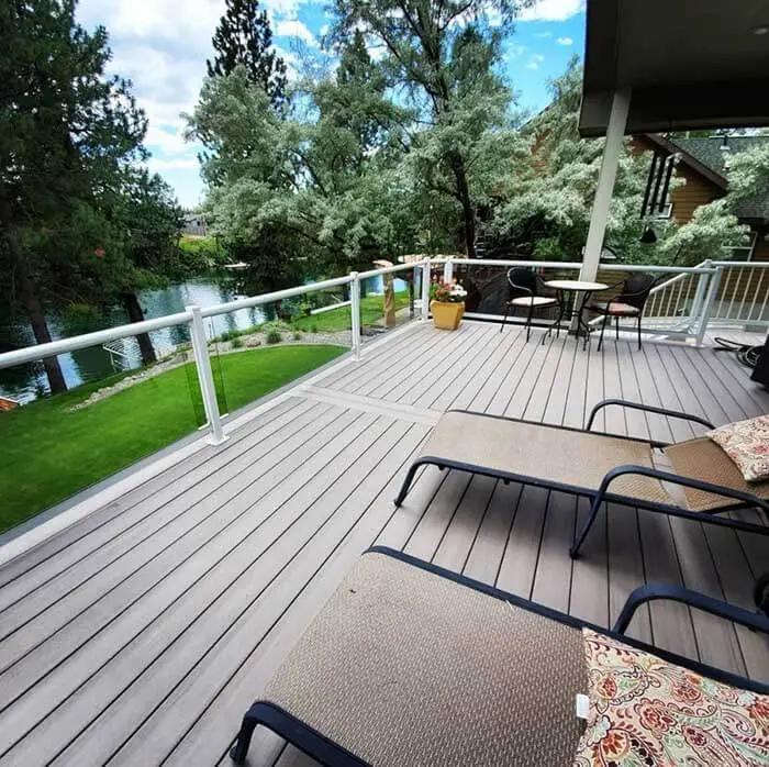 Deck balcony near river with framed glass railing and lounge chairs.