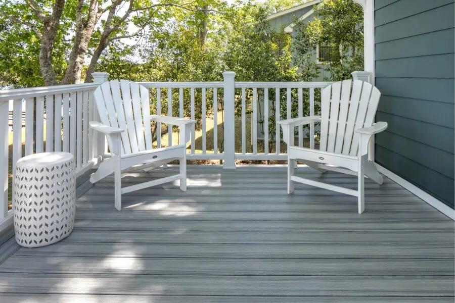 Gray Trex composite deck with white composite railing and two white lawn chairs and a small drink table.
